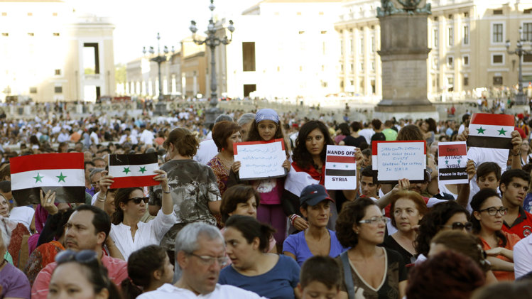 People hold Syrian flags and signs against a possible attack to Syria, prior to the start of a vigil for peace attended by Pope Francis in St. Peter's Square at the Vatican, Saturday, Sept. 7, 2013. Tens of thousands of people have answered Pope Francis' call and massed in St. Peter's Square for a 4-hour-long prayer vigil for peace in Syria. It was believed to be one of the first, and certainly the largest popular rally in the West against U.S.-led plans to strike Syria following the Aug. 21 chemical weapons attack near Damascus. (AP Photo/Riccardo De Luca)